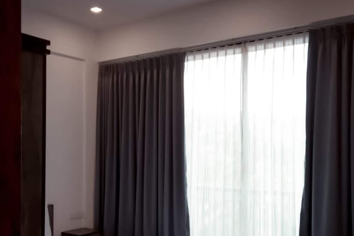 A room with a large window covered by grey curtains, a visible door, and a ceiling light.