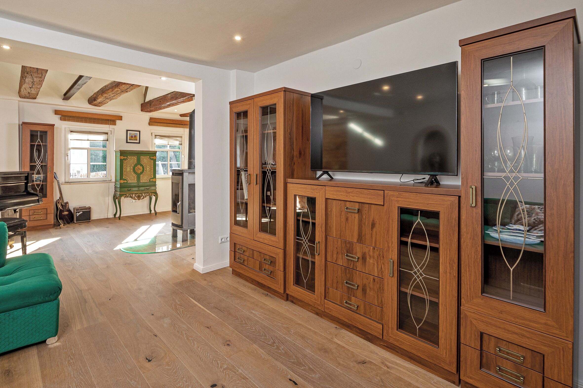 A spacious living room with a large wooden cabinet, a green sofa, and a piano.