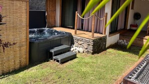 A hot tub in a backyard with a thatched roof, stone walls, and a wooden deck. - Les Vavangues 2 (Saint-Paul)