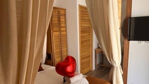 A hotel room with a bed, a television, wooden doors, and curtains. - Les Vavangues 2 (Saint-Paul)