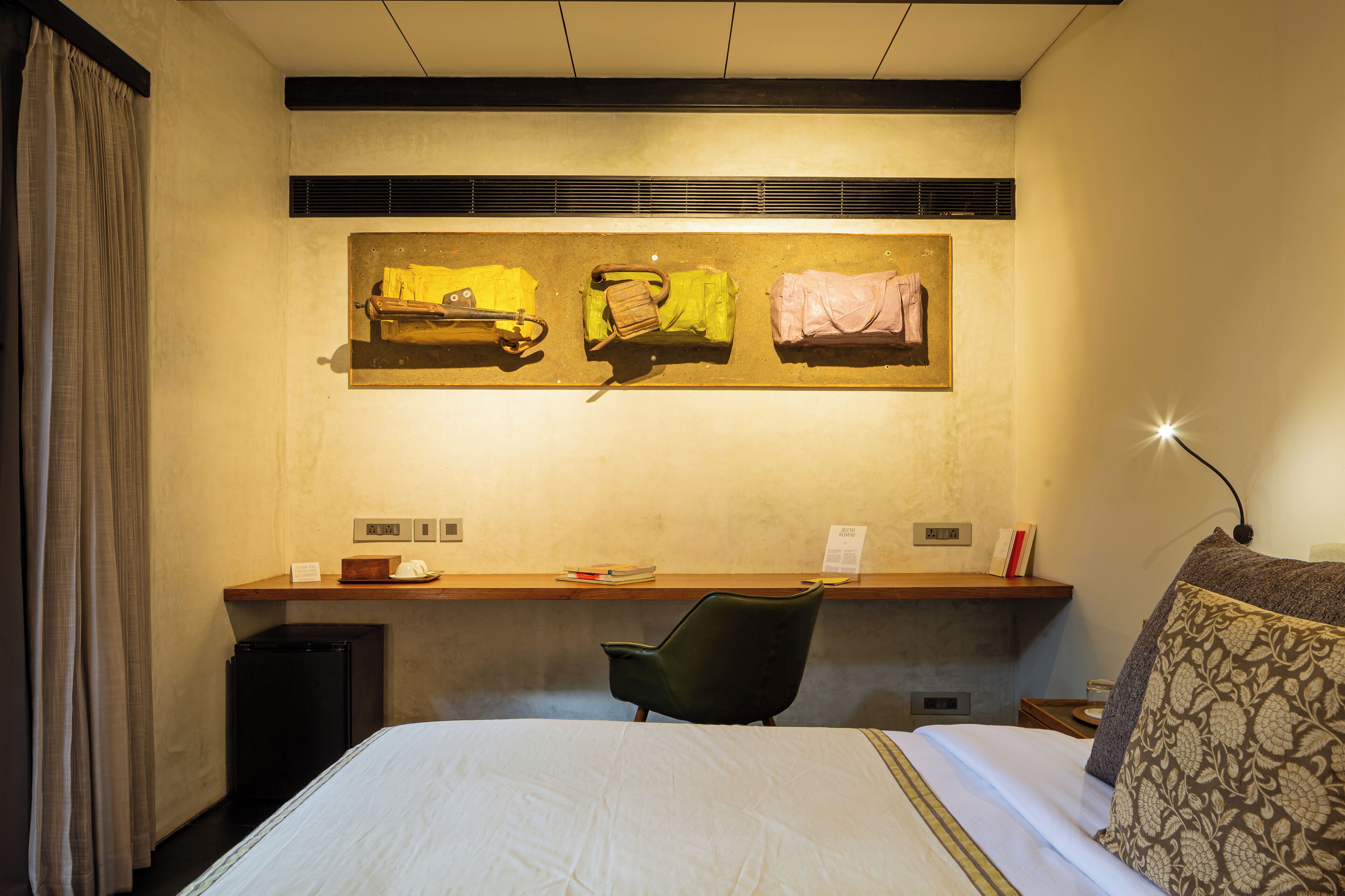 A hotel room with a bed, a desk, a chair, and a painting on the wall.
