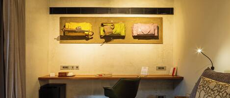 A hotel room with a bed, a desk, a chair, and a painting on the wall.