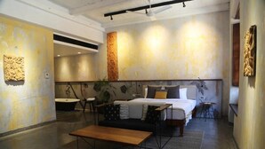 Una habitación de hotel moderna con una cama grande, una mesita, un sofá, una bañera y una obra de arte colgada en la pared.