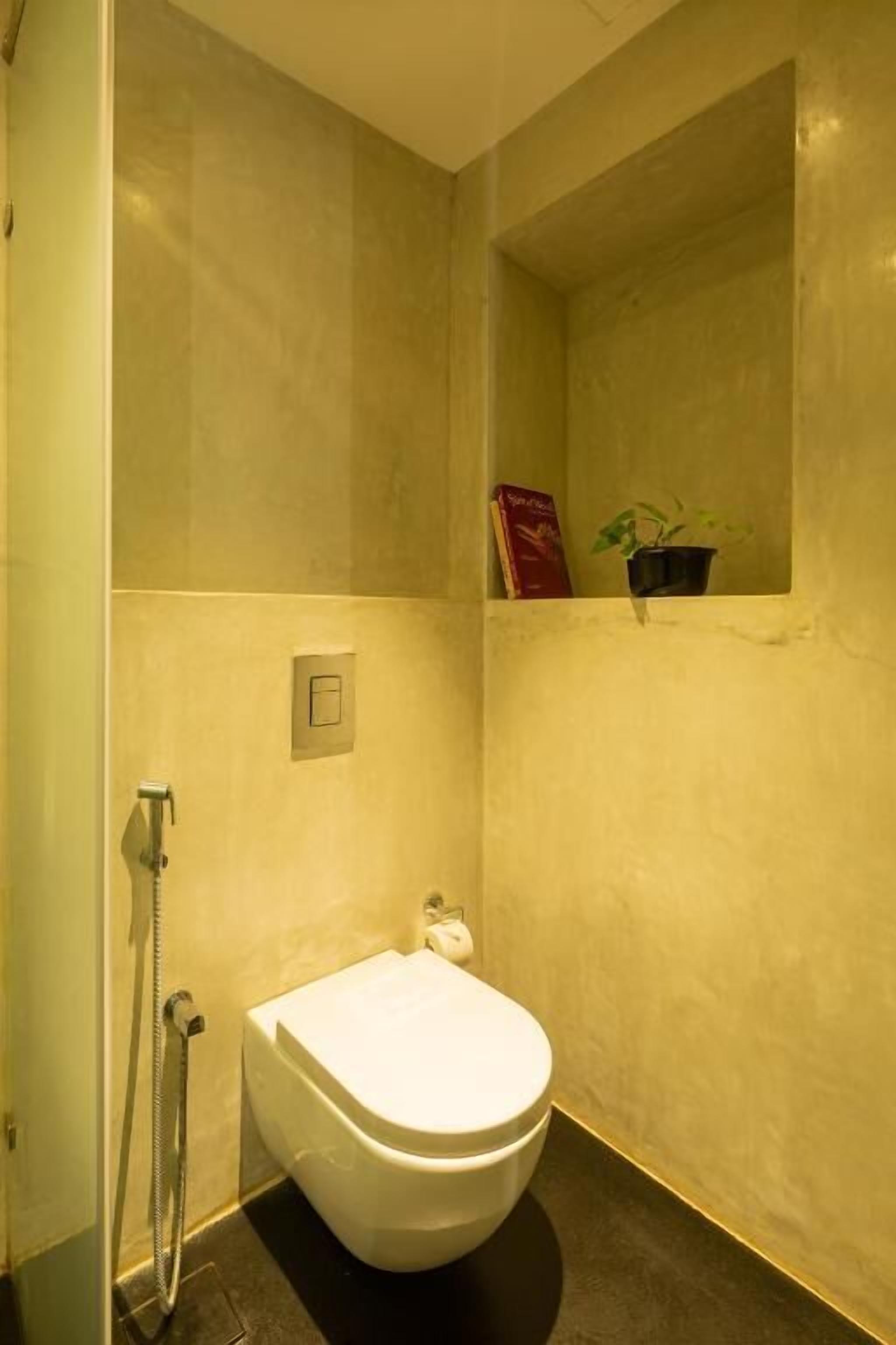 Et badeværelse med toilet, bruser og en lille hylde med en bog og en plante.