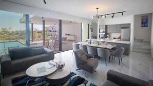 A modern living space with a dining area, kitchen, and a large glass door leading to a balcony. - Protaras Aqua Pearl Villa AQ12 (Paralimni)