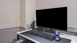 Egy szállodai szoba íróasztallal, számítógép-monitorral, billentyűzettel, egérrel és kávéfőzővel.