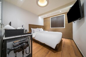 Een moderne hotelkamer met een groot bed, een aan de muur bevestigde televisie en een klein bureau met stoel.