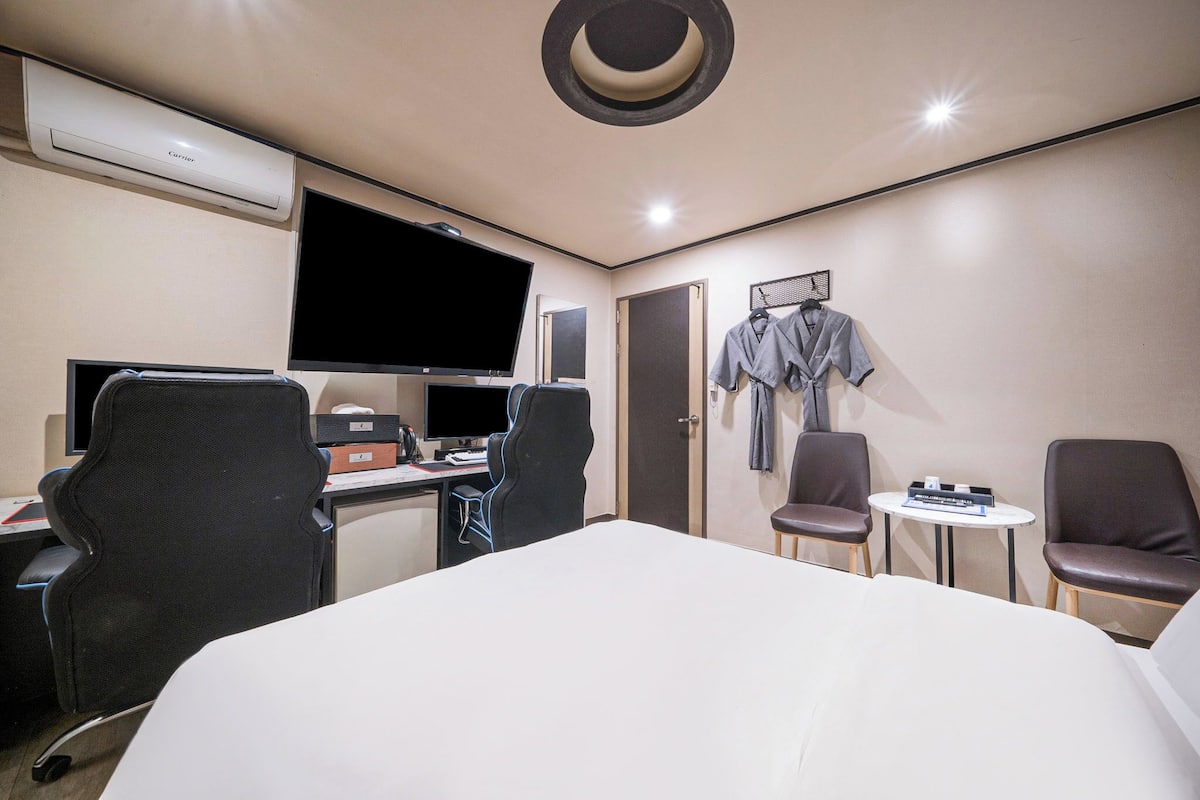 A hotel room with a bed, desk, computer, chairs, and a TV.