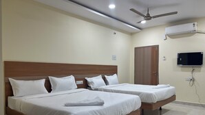 Une chambre d’hôtel avec deux lits, un ventilateur de plafond, un appareil de climatisation et un téléviseur fixé au mur.