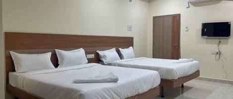 Une chambre d’hôtel avec deux lits, un ventilateur de plafond, un appareil de climatisation et un téléviseur fixé au mur.