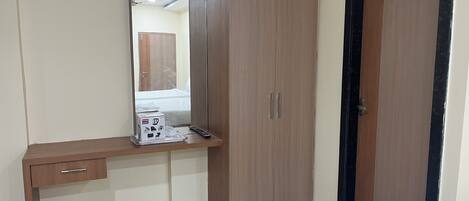 Een kamer met een houten garderobe, een spiegel, een bureau met een afstandsbediening en een deur.