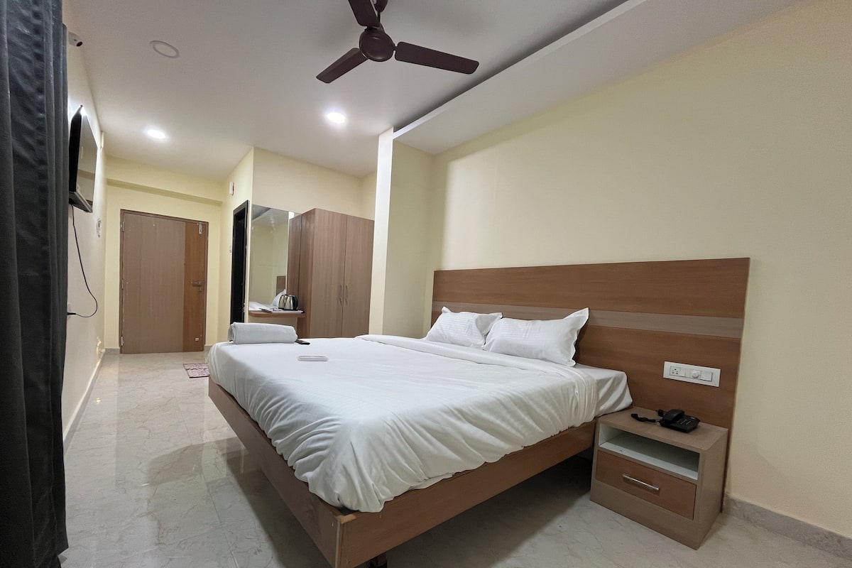 Een slaapkamer met een houten bed, een nachtkastje, een kledingkast, een plafondventilator en een spiegel.