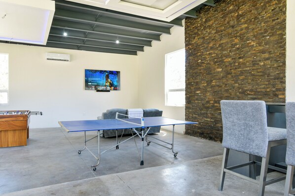 Una mesa de ping pong en una habitación con pared de ladrillo, un sofá y una mesa de fútbol de mesa.