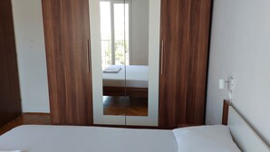 Une chambre dotée d’une grande armoire, d’un lit et donnant sur un balcon.