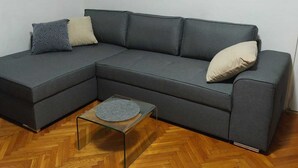 Un canapé modulable avec deux coussins, une table basse en verre et un parquet en bois à motifs chevrons.