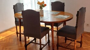 Un coin repas comprenant une table ronde en bois, quatre chaises rembourrées, un vase avec des fleurs et une horloge murale.