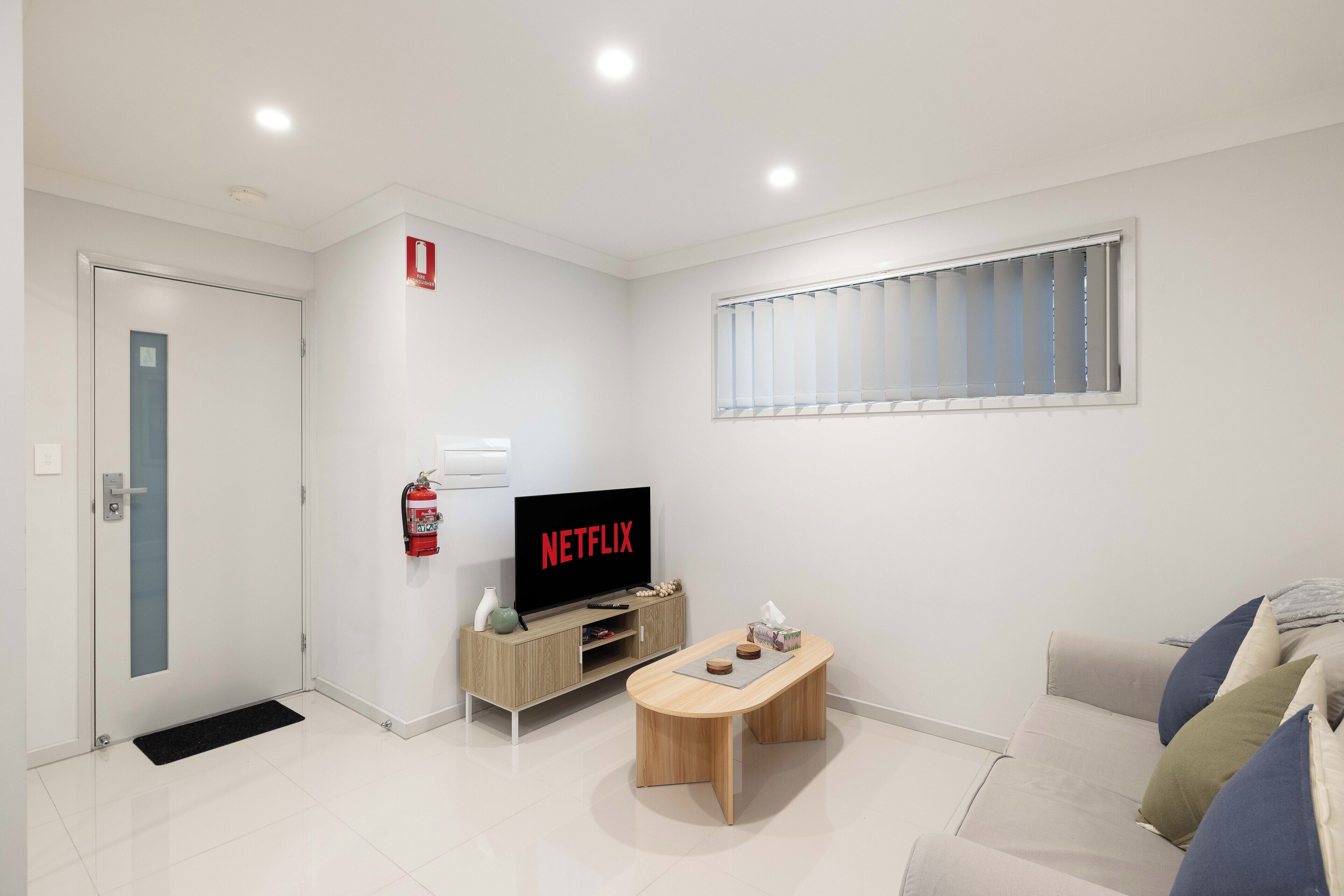Una sala de estar moderna con una televisión de pantalla plana, una mesa de centro de madera, un sofá y una ventana con persianas.