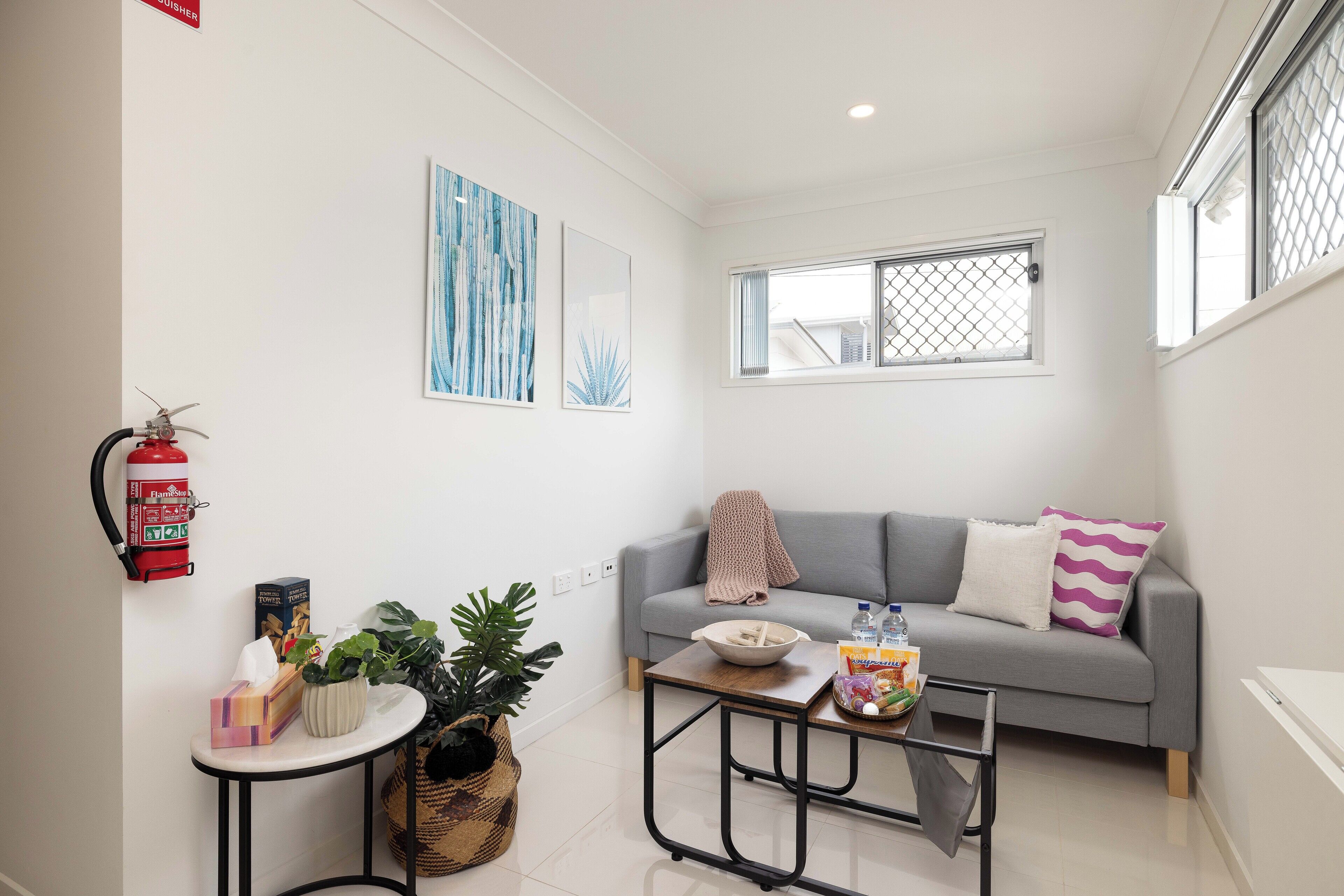 A modern living room with a grey sofa, a small coffee table, and a fire extinguisher mounted on the wall.