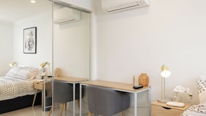 A modern bedroom with a bed, a desk, two chairs, a nightstand, and a mirror. - Smart Suites Self Check-in Apartments - 14A Freney (Rocklea)