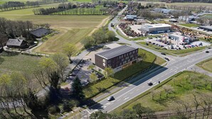 Luchtbeeld van een modern gebouwencomplex met meerdere parkeerplaatsen, wegen en omliggende groene velden.