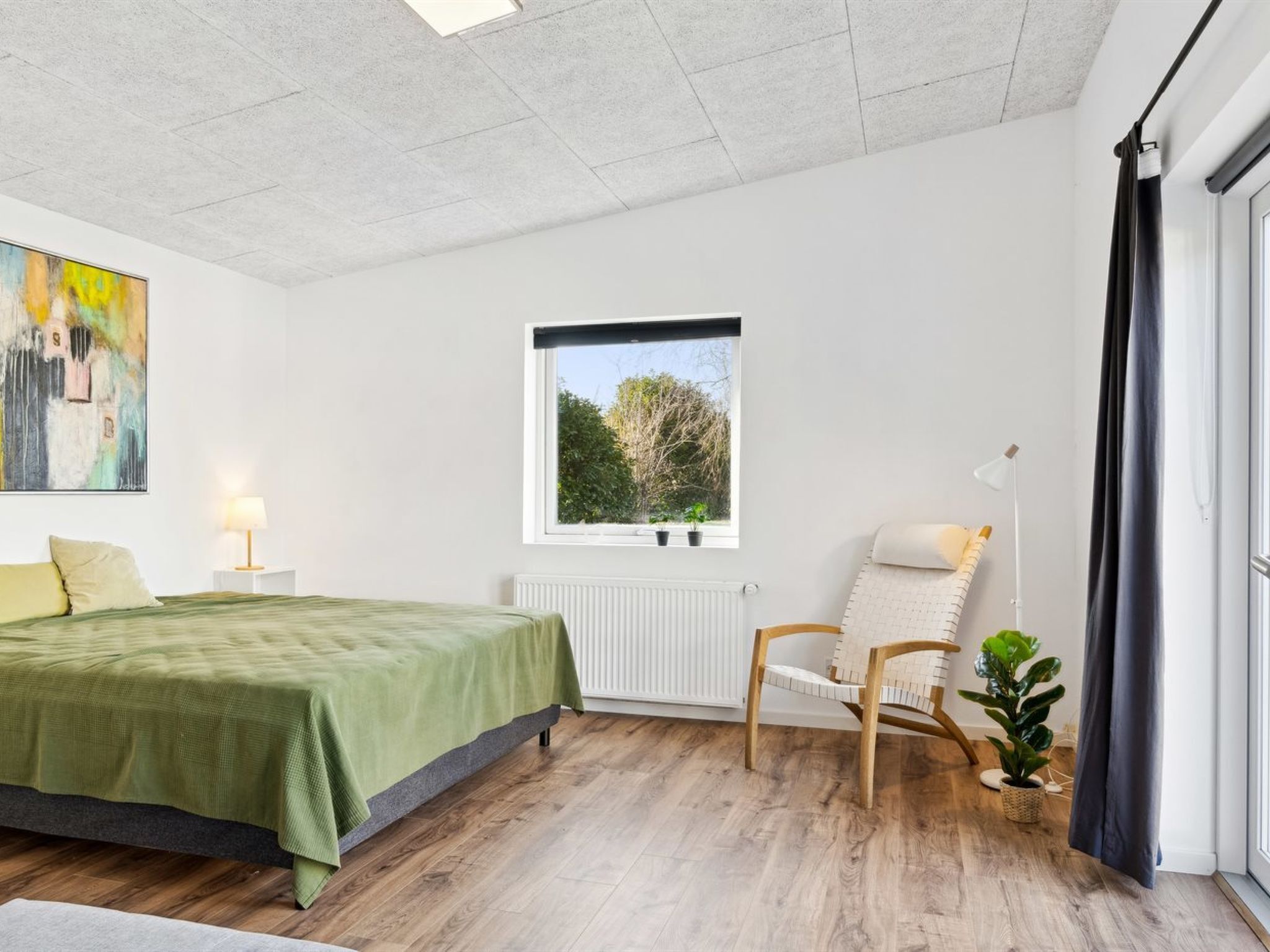Ein Schlafzimmer mit einem Bett, einem Sessel, einem Fenster und einer Heizung.