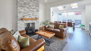 A spacious living room with a fireplace, leather sofas, a wooden coffee table, and a dining area with natural light from skylights. - Host Stay Peasholm Place (Scarborough)