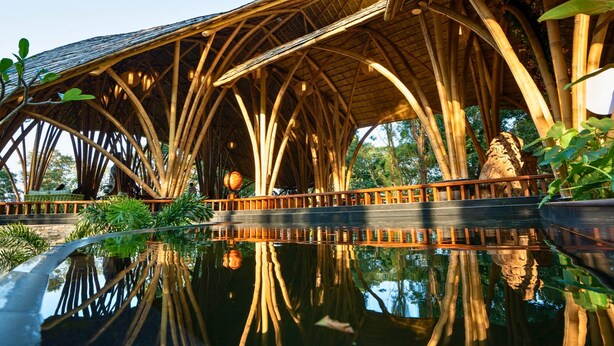 Estrutura de bambu com uma superfície aquática refletora à frente.