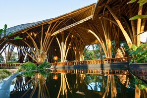 A bamboo structure with a reflective water surface in front. - The Leela Coorg Forest Sanctuary (Horur)