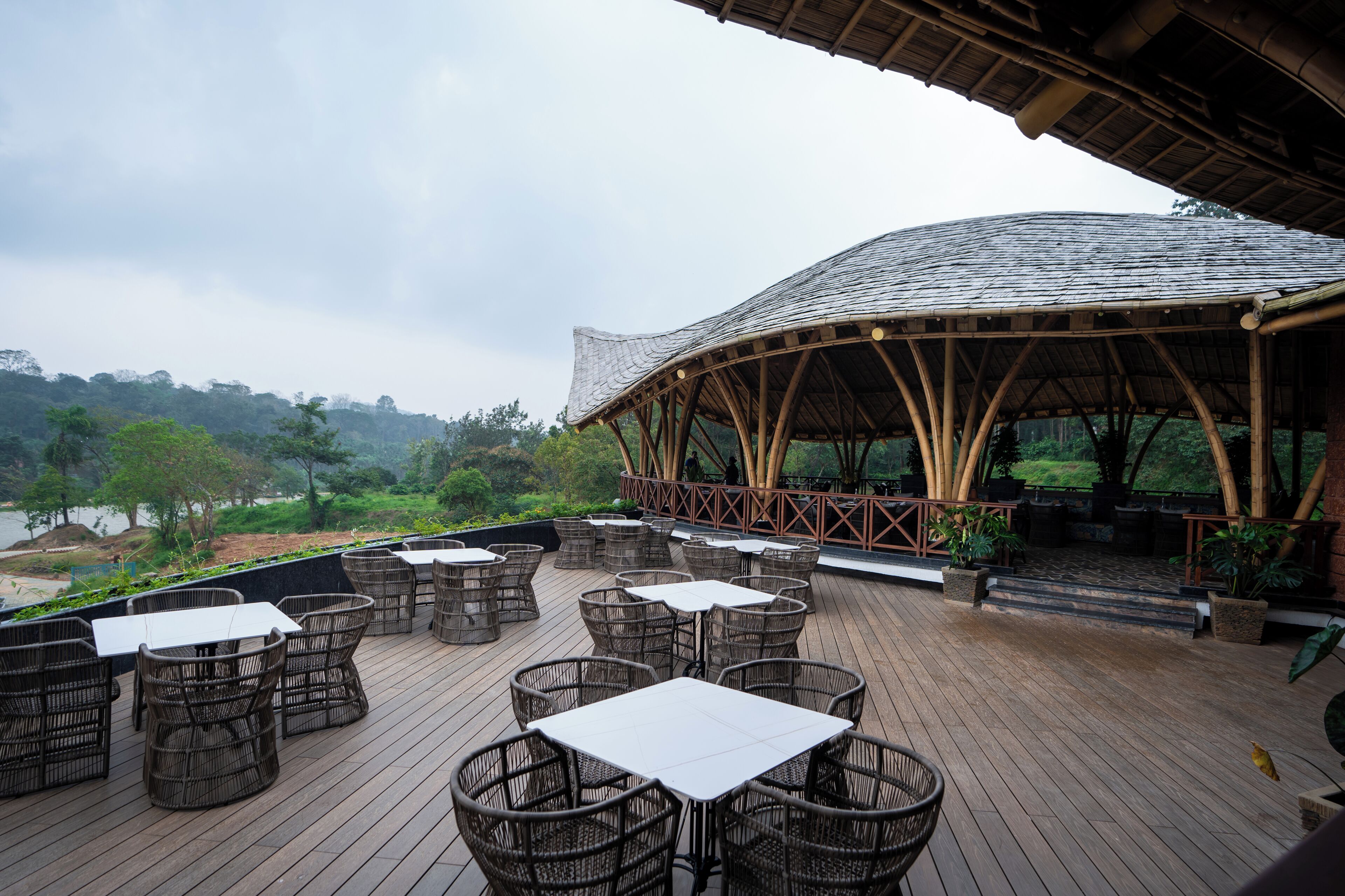 An outdoor dining area with wicker furniture and a covered seating area overlooking a natural landscape.