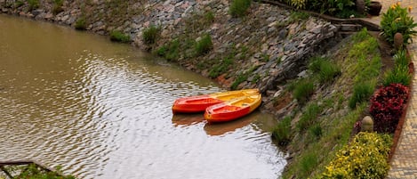 A river with two kayaks, a stone wall, and a pathway with plants.