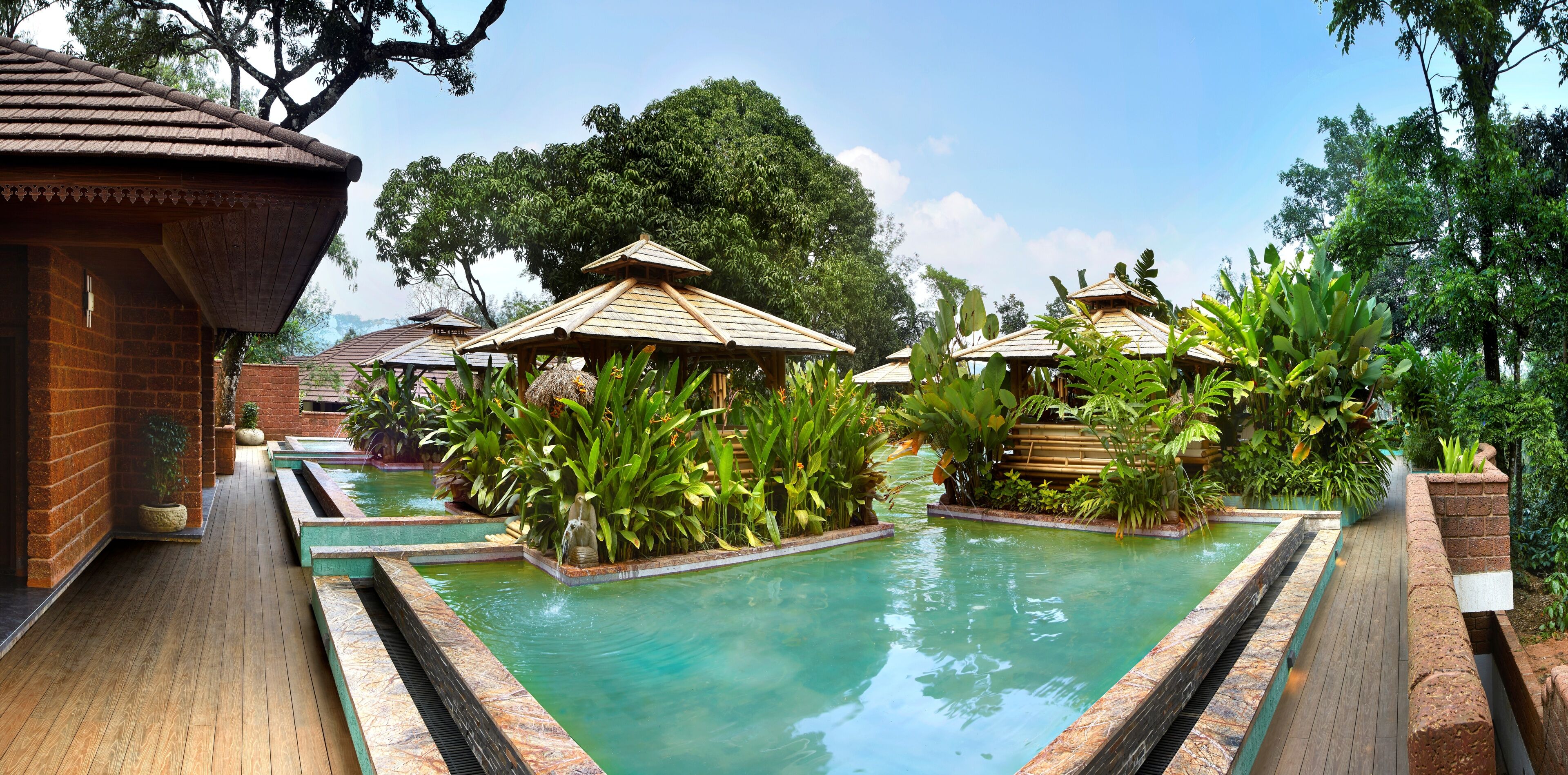 A pool area with wooden deck, potted plants, and thatched-roof structures.