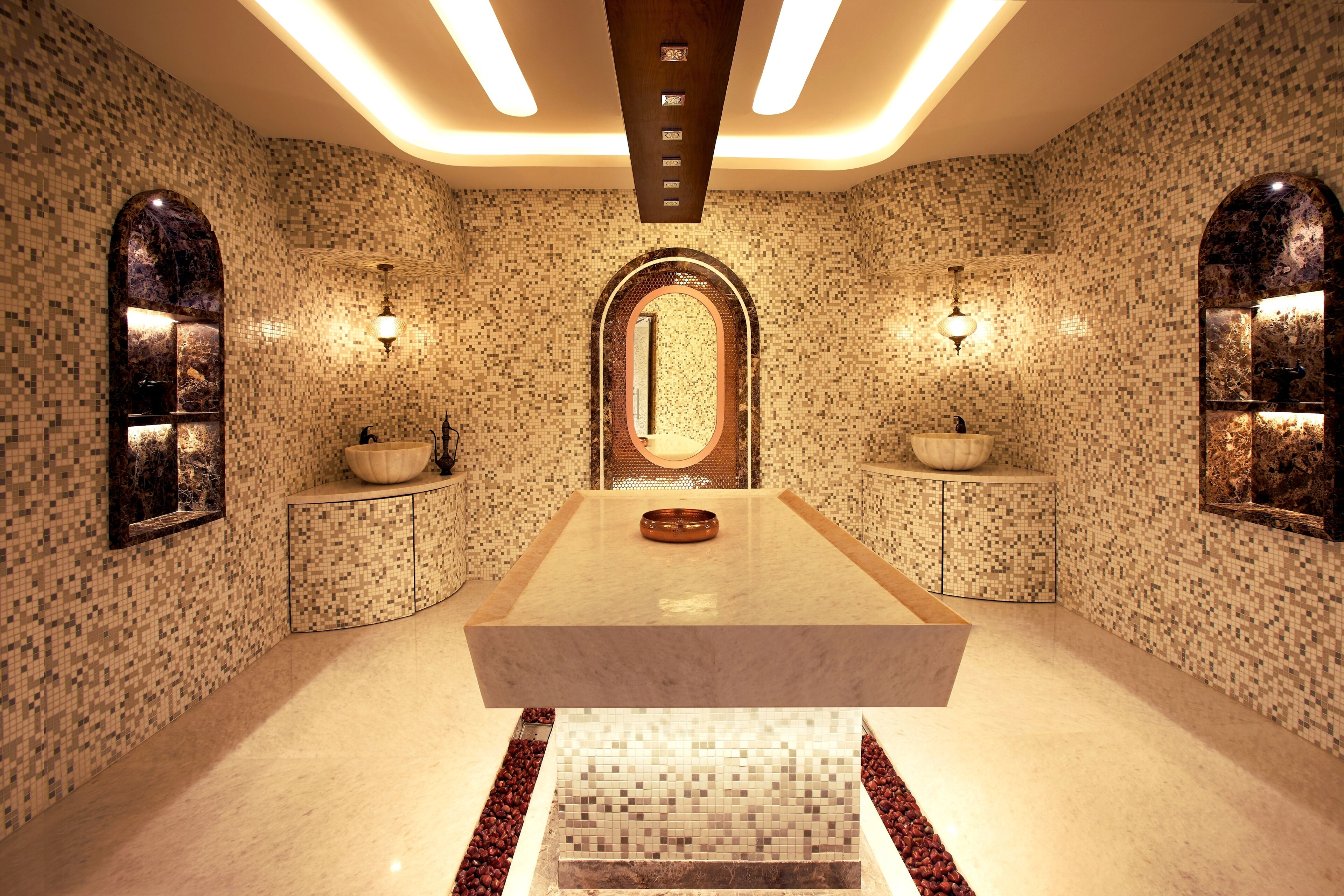 A luxurious bathroom with mosaic walls, a central marble sink, and a large mirror.