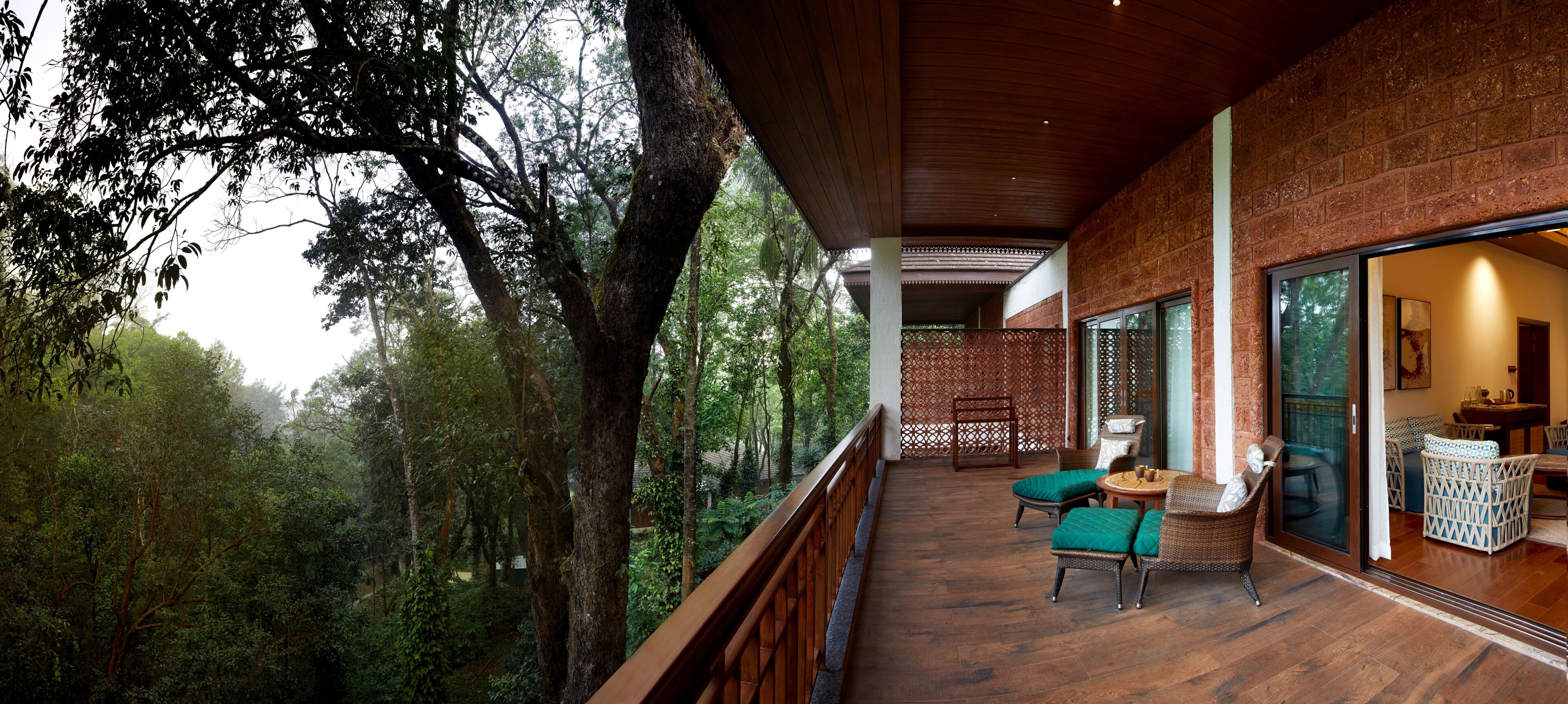 A balcony with wicker furniture, a wooden floor, and a view of a forested area.