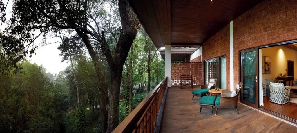 Un patio in legno con vista su una foresta, un'area pranzo con sedie e un'ampia finestra.