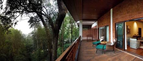 A wooden deck with a view of a forest, a dining area with chairs, and a large window.