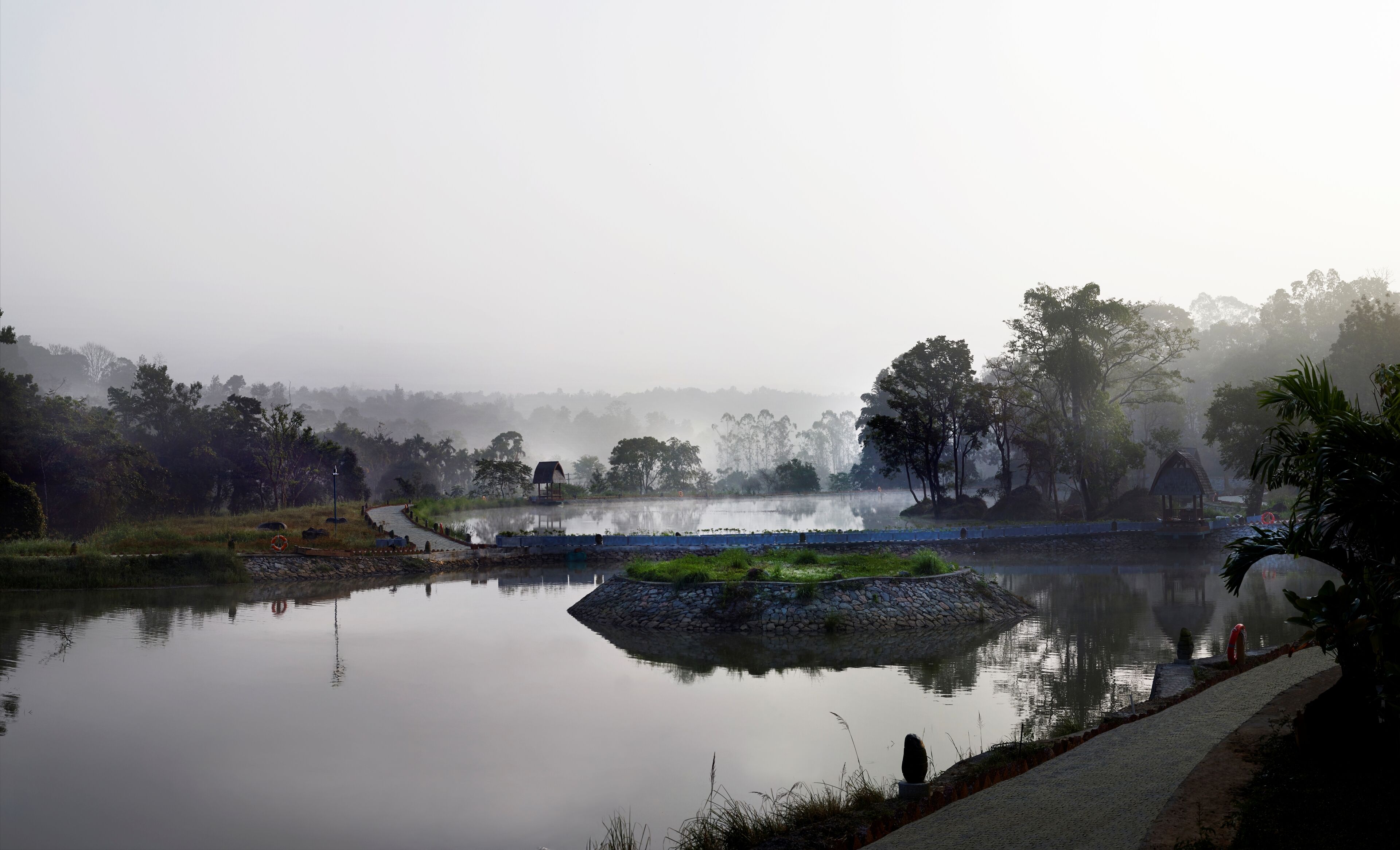 A serene lake with a stone pathway, a gazebo, and lush greenery.