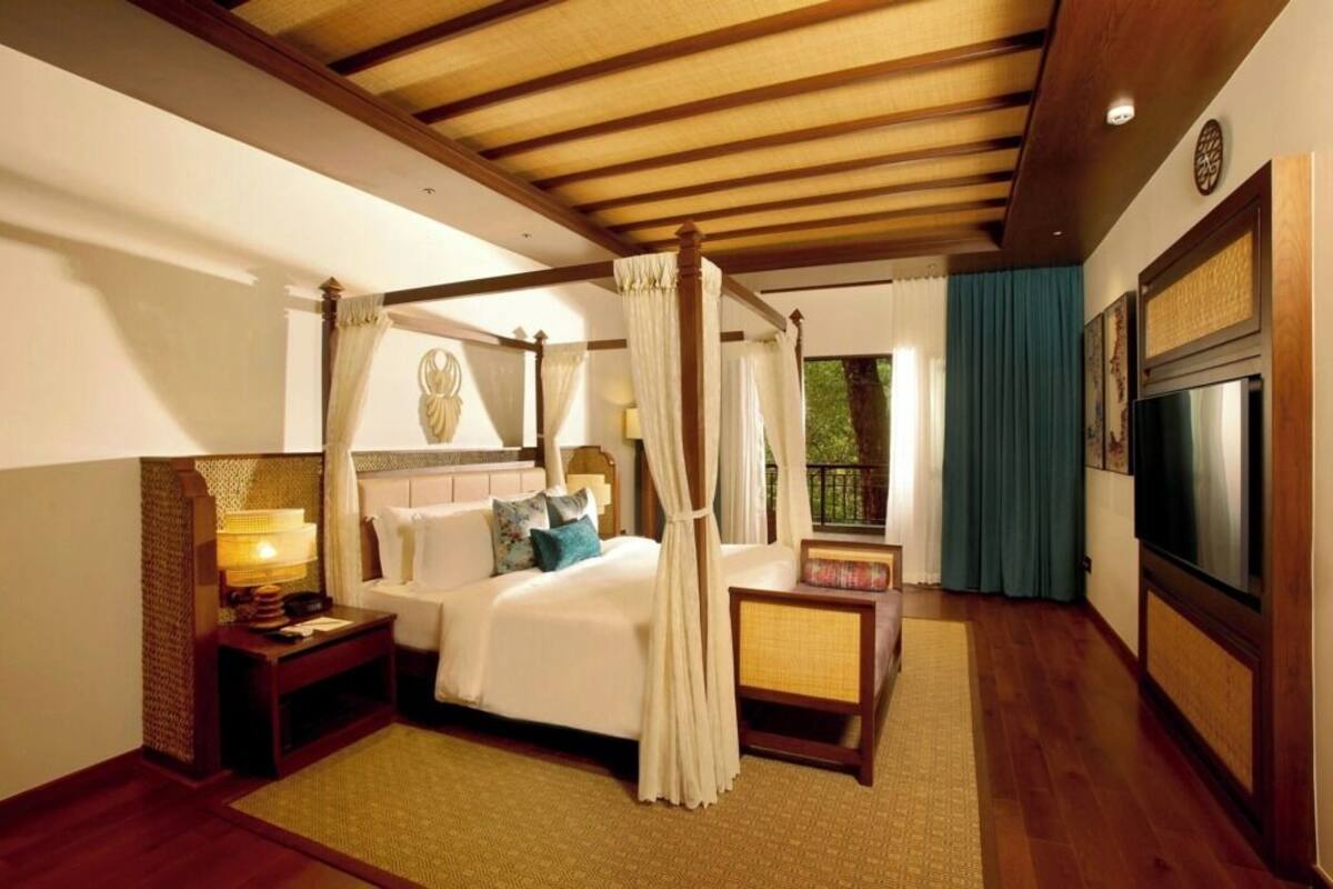Una cama con dosel y cortinas, un televisor y un ventanal grande con cortinas.