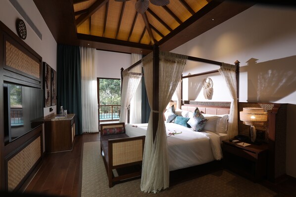 A bedroom with a four-poster bed, a bedside table, a nightstand, a TV, and a view of the outdoors. - The Leela Coorg Forest Sanctuary (Horur)