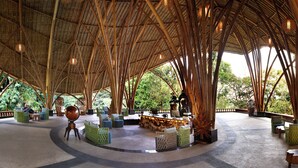 Um pavilhão ao ar livre com estruturas de bambu, áreas de estar e um bar central.