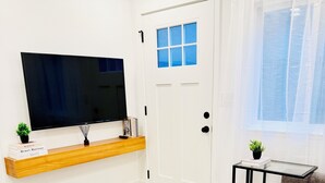 A modern living room with a flat-screen TV, a bookshelf, a sofa, and a small table. - Modern 2BR Near SJC | W/D | FirePit | Free Parking (San Jose)