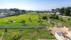 Un camp verd amb una tanca blanca, un parc de swings i una zona pavimentada amb jardineres.