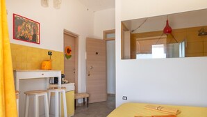 Un dormitori petit i funcional, amb llit, escriptori petit i tamborets, mirall i porta que condueix a una altra habitació.