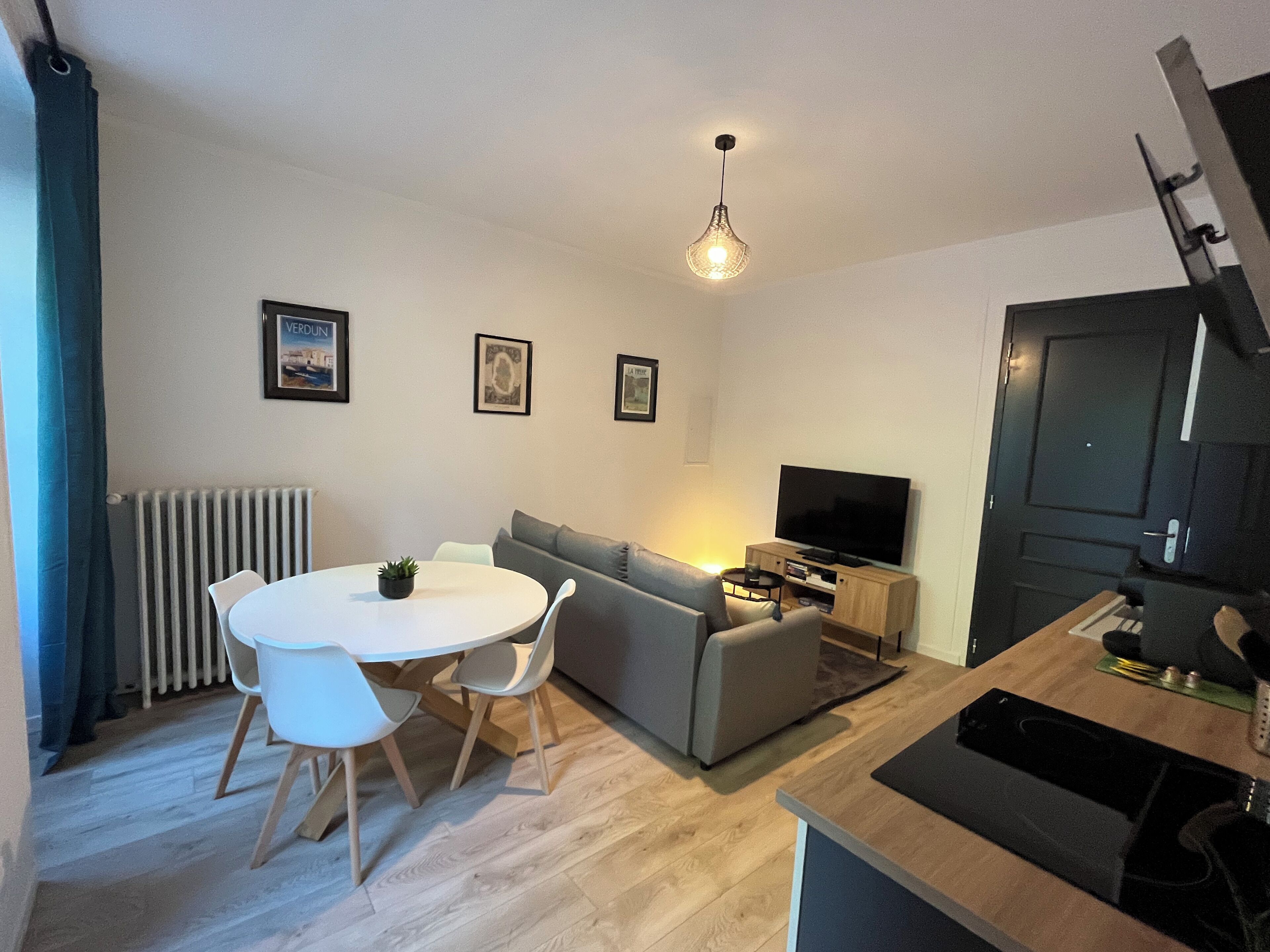 Een moderne woonkamer met een eettafel, een grijze bank en een televisie op een houten dressoir.