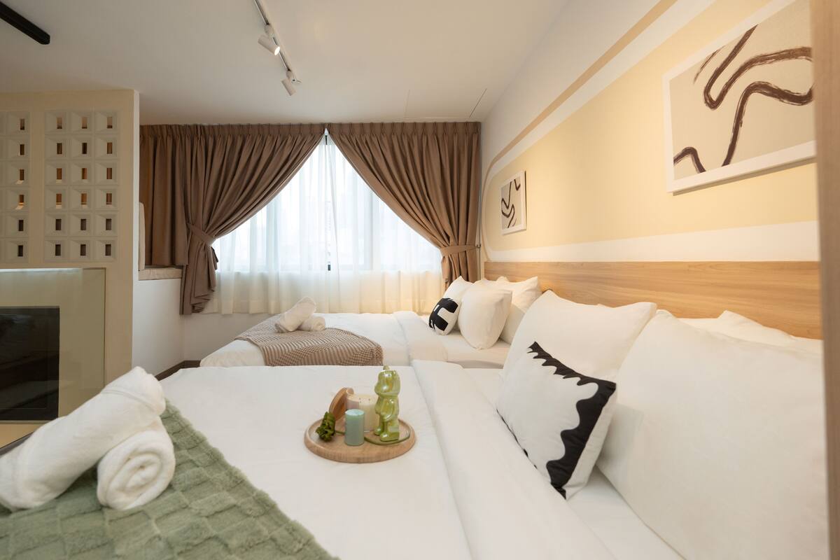 A hotel room with a bed, a sofa, a wooden headboard, a wall art piece, and a window with curtains.