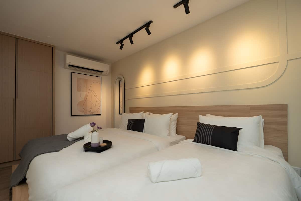 A hotel room with two beds, a wooden wardrobe, an air conditioning unit, and a framed abstract artwork on the wall.