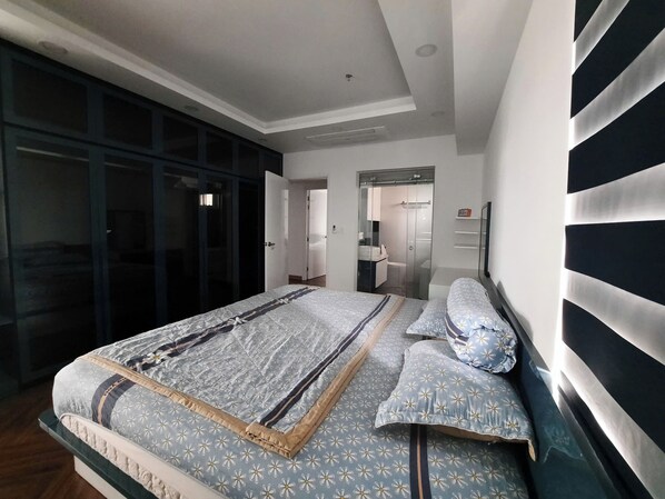 A bedroom with a large bed, a wardrobe, and a bathroom visible through an open door. - Cosmo City (Ho Chi Minh City)