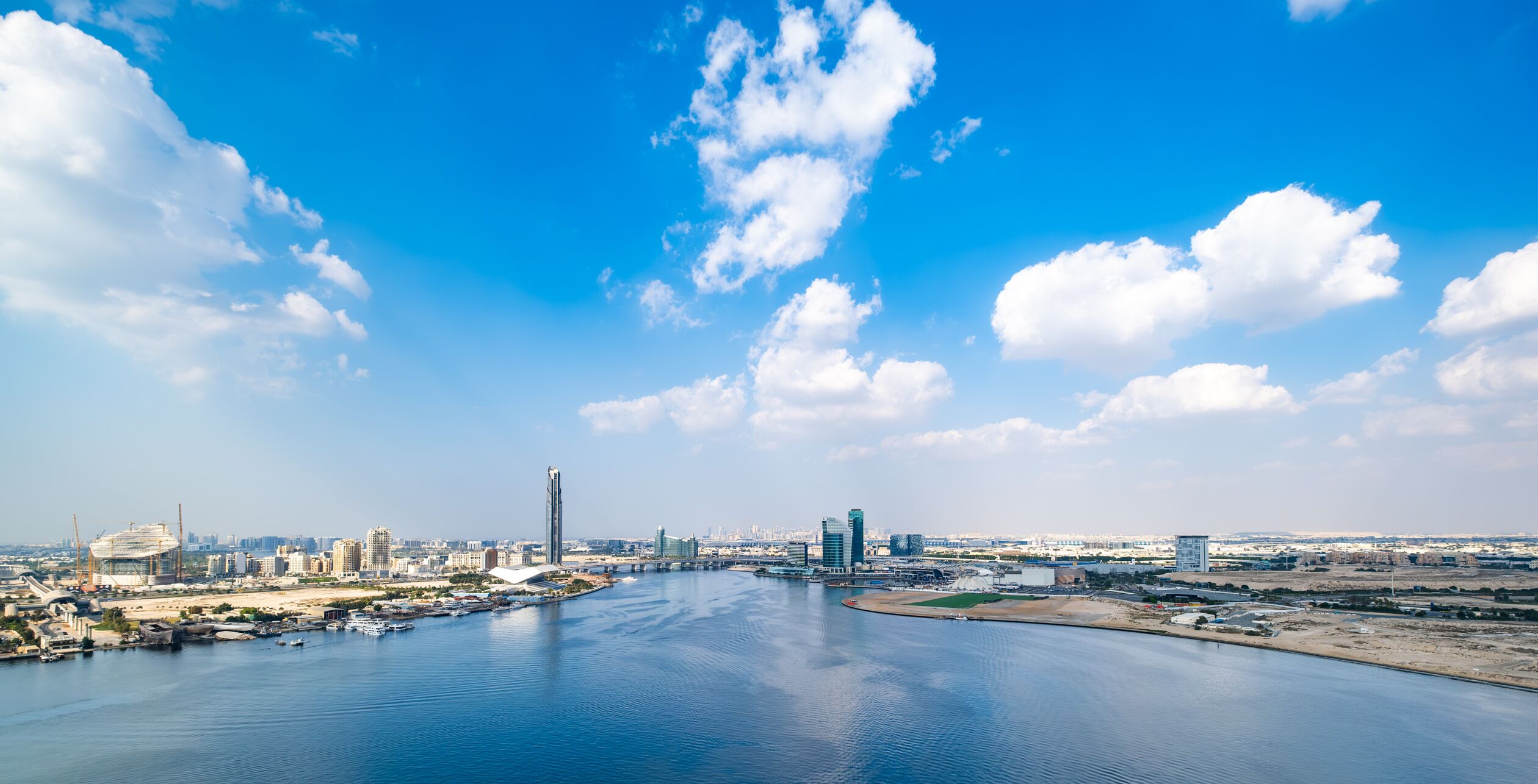 A waterfront cityscape with modern buildings, a prominent tower, and a marina.