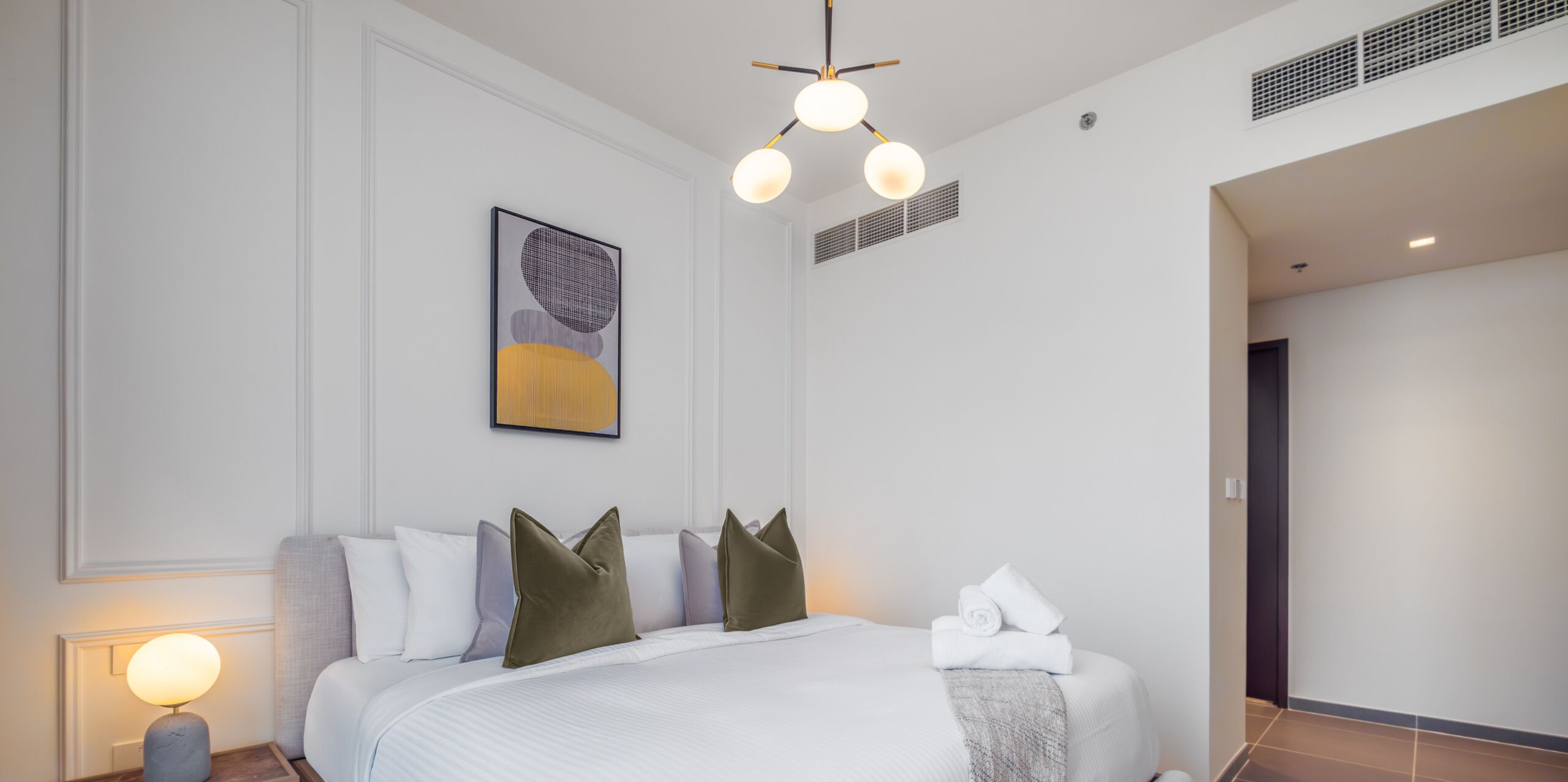 Una camera d'albergo moderna con un letto grande, un comodino con una lampada, un lampadario e un quadro appeso al muro.
