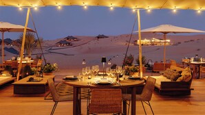 Een terras met eethoek en uitzicht op een woestijnlandschap, tafels gedekt voor een diner, met sfeerverlichting.