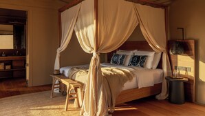 Een hemelbed met houten hoofdeinde, nachtkastjes en een bankje.